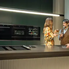 Para w nowoczesnej kuchni, przy wyspie z płytą indukcyjną i zintegrowanym okapem, delektuje się napojami.