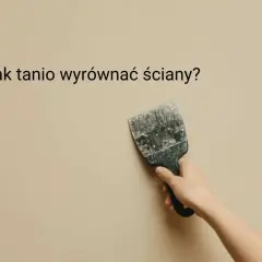 Dłoń trzyma szpachelkę przy lekko nierównej, beżowej ścianie. Jak tanio wyrównać ściany?