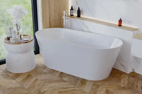 Elegancka wolnostojąca wanna w łazience z drewnianą podłogą ułożoną we wzór jodełki. Obok wanny stoi stolik z kosmetykami i kwiatami.
