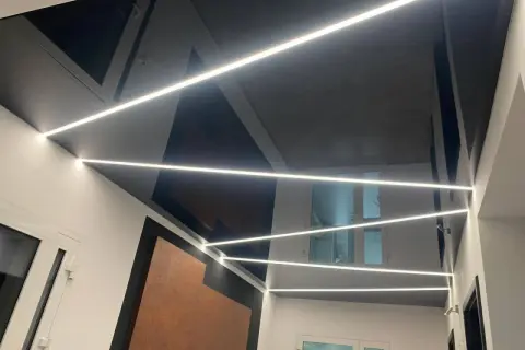 Nowoczesny sufit napinany w salonie z geometrycznymi wzorami i liniowym oświetleniem LED.