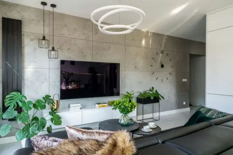 Nowoczesny salon z dużym telewizorem na tle betonowej ściany. Wygodna, czarna kanapa zaprasza do relaksu.