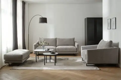 Nowoczesny salon z dwiema sofami, fotelem i pufą. W centrum dwie okrągłe ławy.