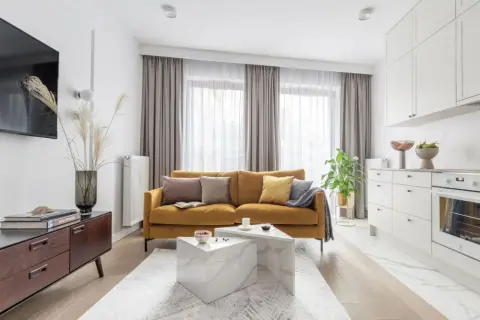 Musztardowa kanapa inspiracje: przytulny salon z nowoczesną kuchnią. Miękkie poduszki i pled dodają ciepła.
