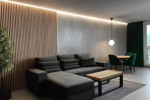 Nowoczesny **styl industrialny salon loft** z szarą sofą, drewnianą ścianą i zielonymi akcentami.